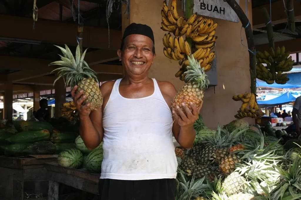 Pedagang buah memegang dua nanas di kiosnya